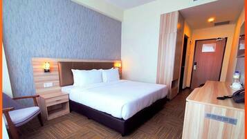 Habitación de hotel con cama, mesita de noche, silla y escritorio con teléfono.