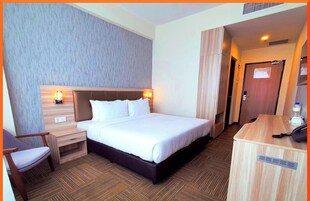 Habitación de hotel con cama, mesita de noche, silla y escritorio con teléfono.