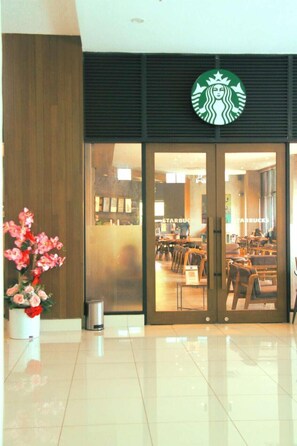 Starbucksin myymälä, jossa on moderni muotoilu. Sen yläpuolella on suuri logo, sisätilat ovat siistit ja niissä on istuimia, ja vasemmalla puolella on ruukussa oleva kasvi.