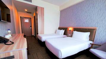 A hotel room with two beds, a desk with a telephone, and a television.