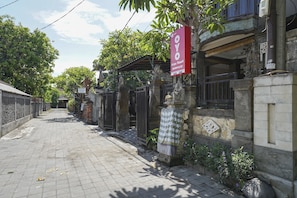 A street view of a residential area with a gated entrance, a red sign, and a stone wall. - OYO 2321 Griya Shanti Homestay (Batubulan)