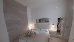 A bedroom with a bed, bedside tables, a mirror, and a small seating area with a tray. - AlbaChiara B&B (Gaeta)
