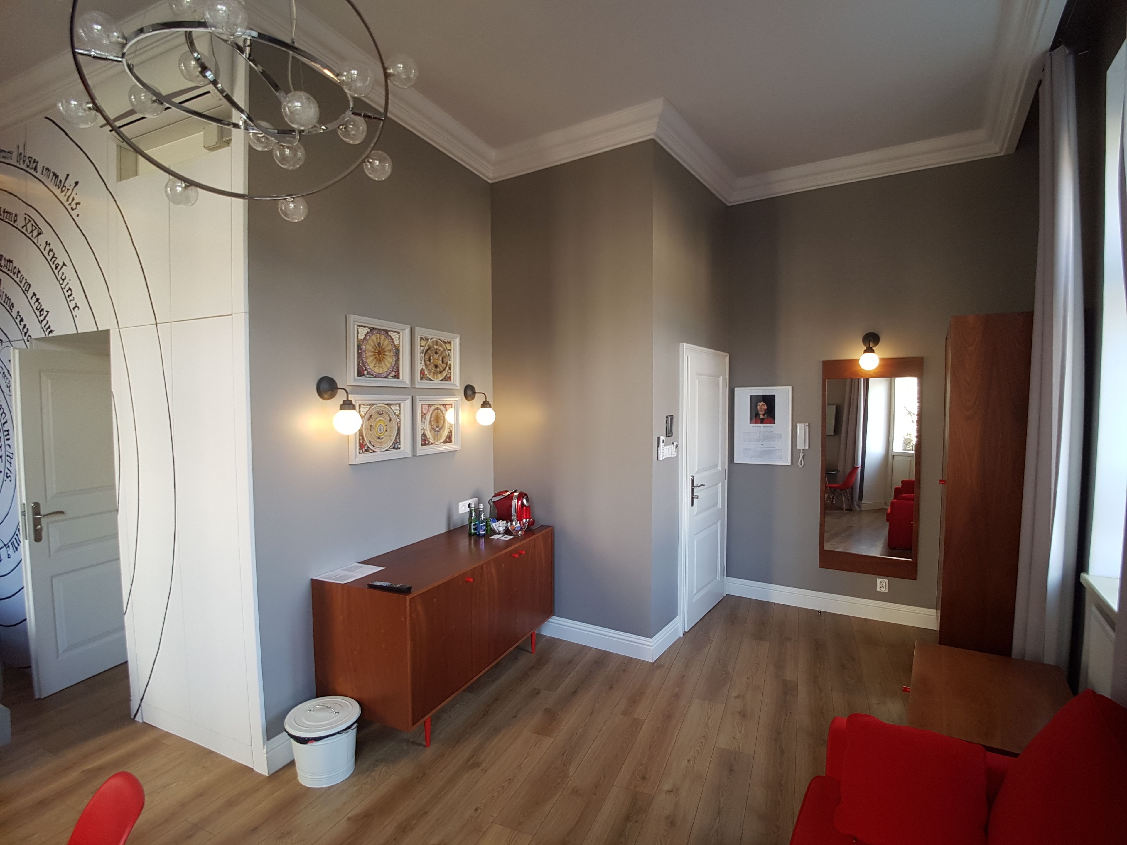 A modern living room with a wooden floor, a red sofa, a wooden cabinet, and a chandelier.