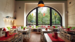 Restaurante com mesas e cadeiras, janelas amplas e luminárias pendentes.