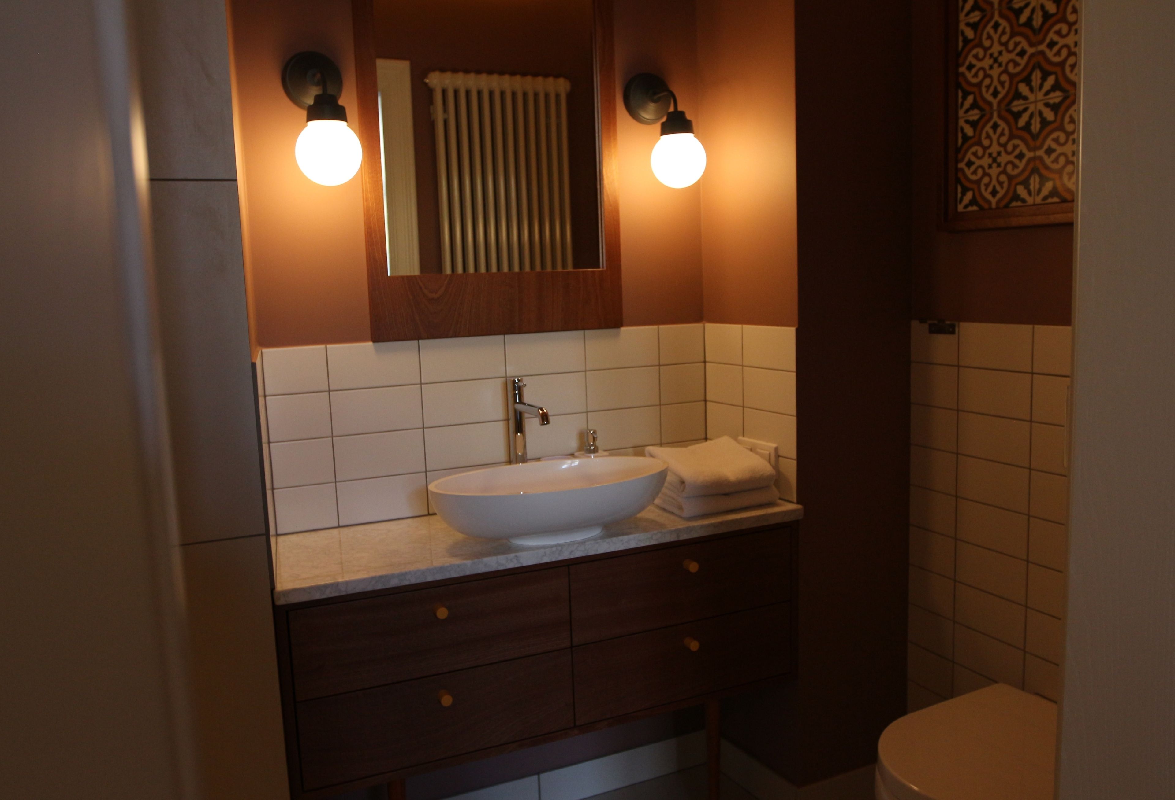 A bathroom with a white sink, dark wooden vanity, two wall-mounted lights, a mirror, and a toilet.
