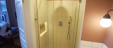 A glass-enclosed shower with a handheld showerhead, a towel rack, and a light fixture.