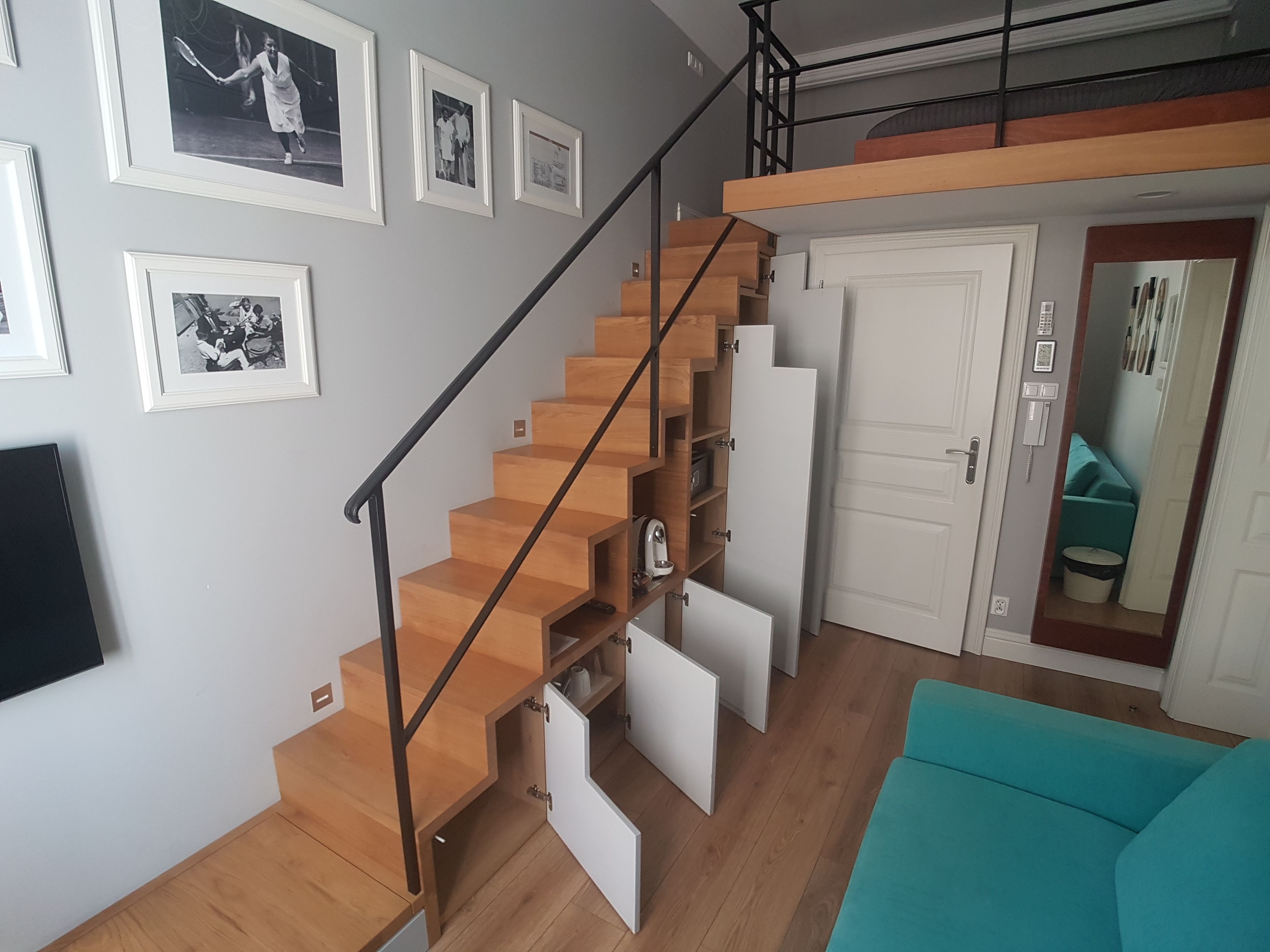 A modern living space with a wooden staircase, a teal sofa, and framed photographs on the wall.