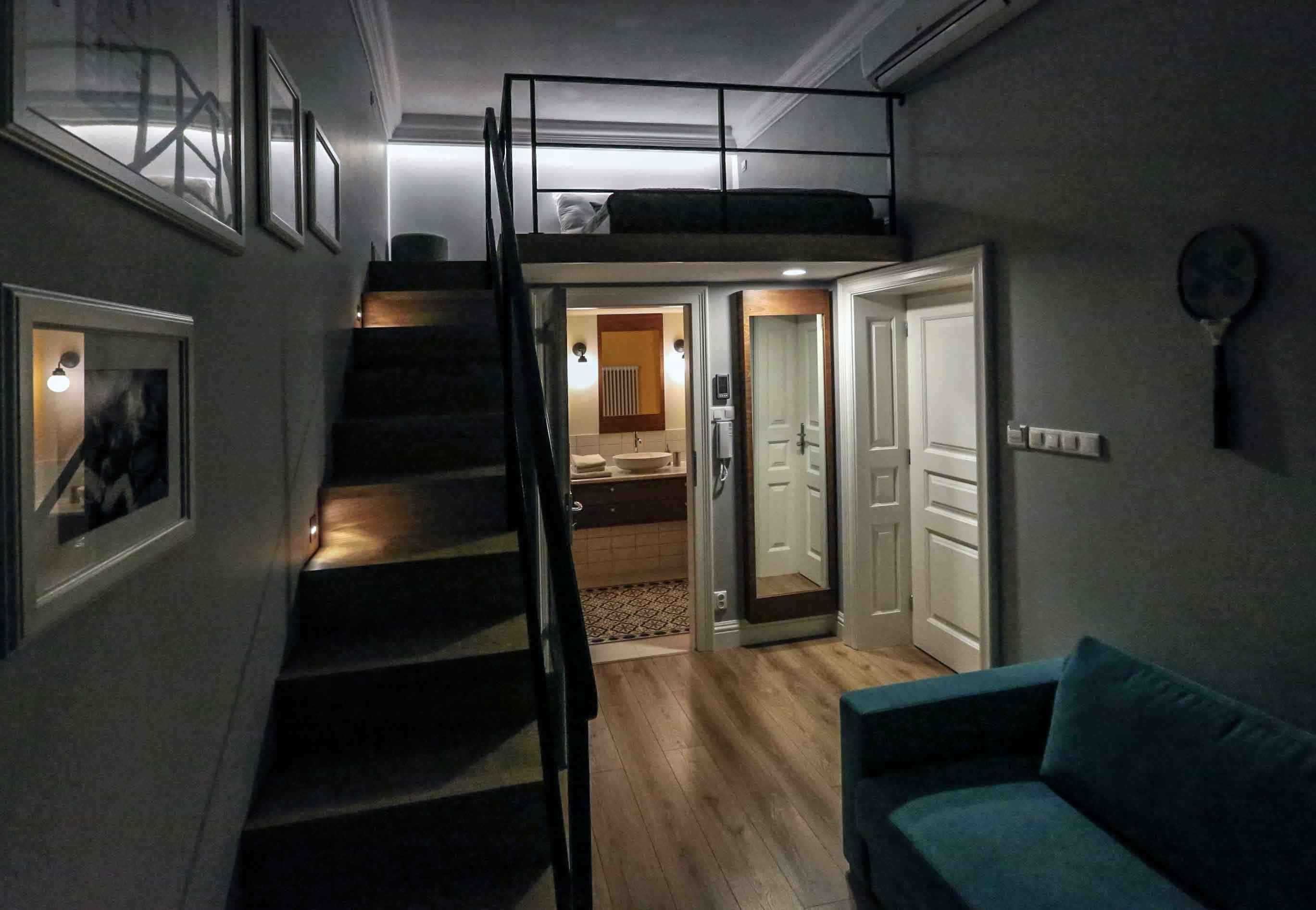 A multi-level living space with a staircase, a bunk bed, a sofa, and a kitchen area.