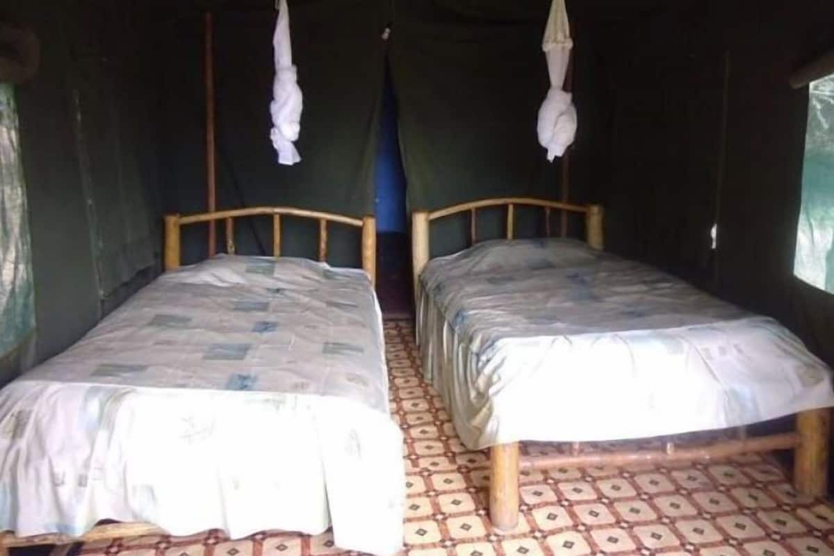 Two single beds with wooden frames and patterned bedding, a tiled floor, and a curtain-covered window.