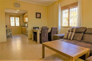 A living room with a sofa, a wooden coffee table, and a dining area with chairs and a table.