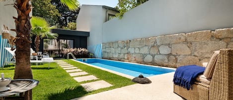Ein moderner Poolbereich im Freien mit einer Steinwand, einer Liege und einem Esstisch.
