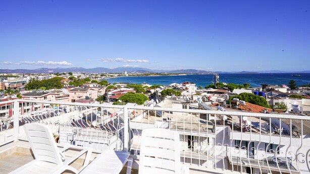 Un balcon avec des chaises blanches et une vue sur un paysage urbain côtier, avec des bâtiments et la mer.