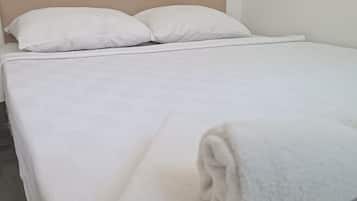 A bed with a beige headboard, white bedding, and a rolled towel on the footboard.