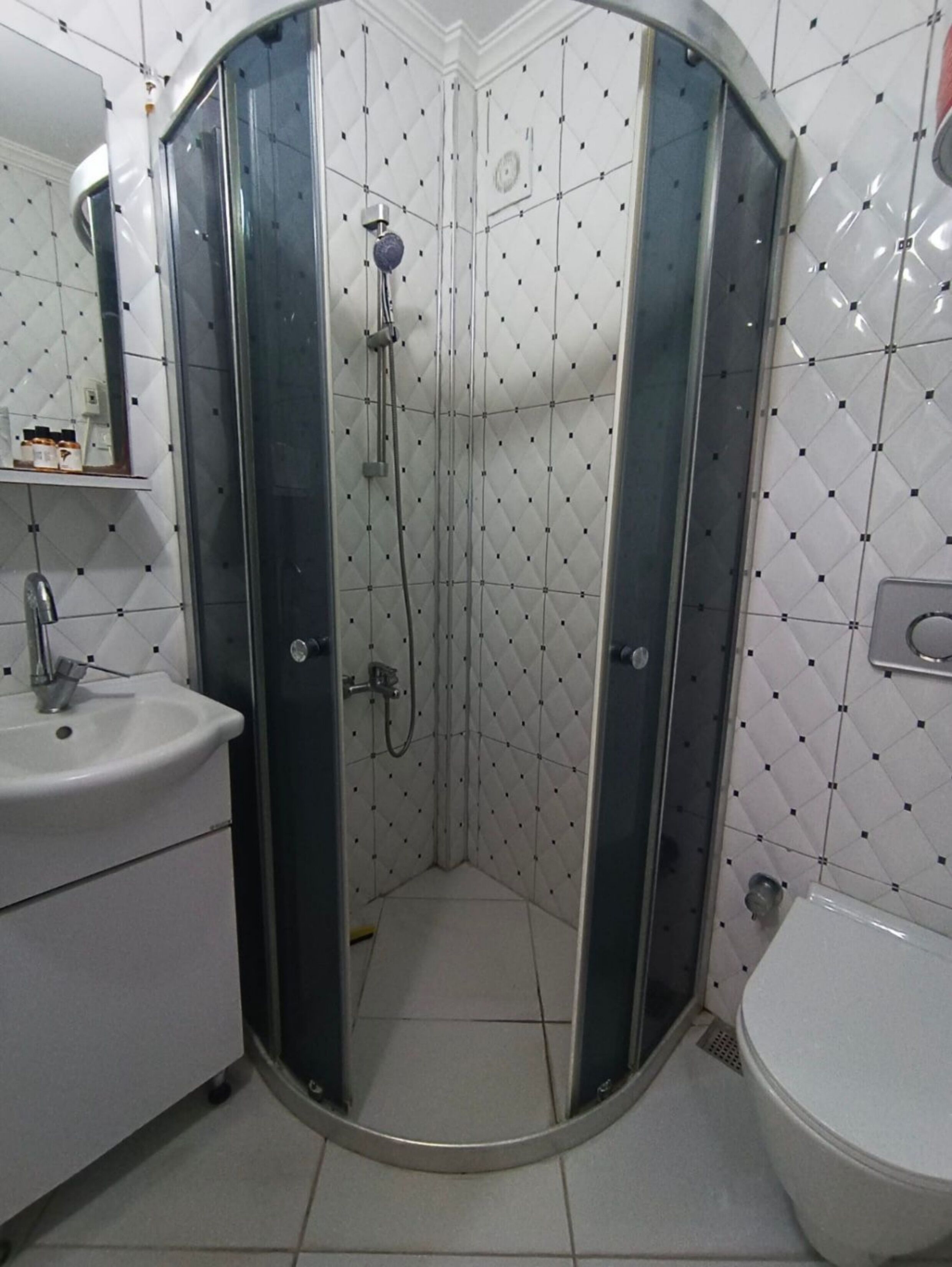 Een douchehoek met glazen deuren, een wastafel en een toilet in een betegelde badkamer.