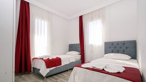 Une chambre d’hôtel avec deux lits, chacun recouvert d’une courtepointe rouge et blanche, et dotée d’une tête de lit grise. Les murs de la chambre sont blancs et le sol est en bois.