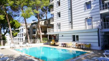 A swimming pool with lounge chairs and a bar area, surrounded by a multi-story building with balconies.