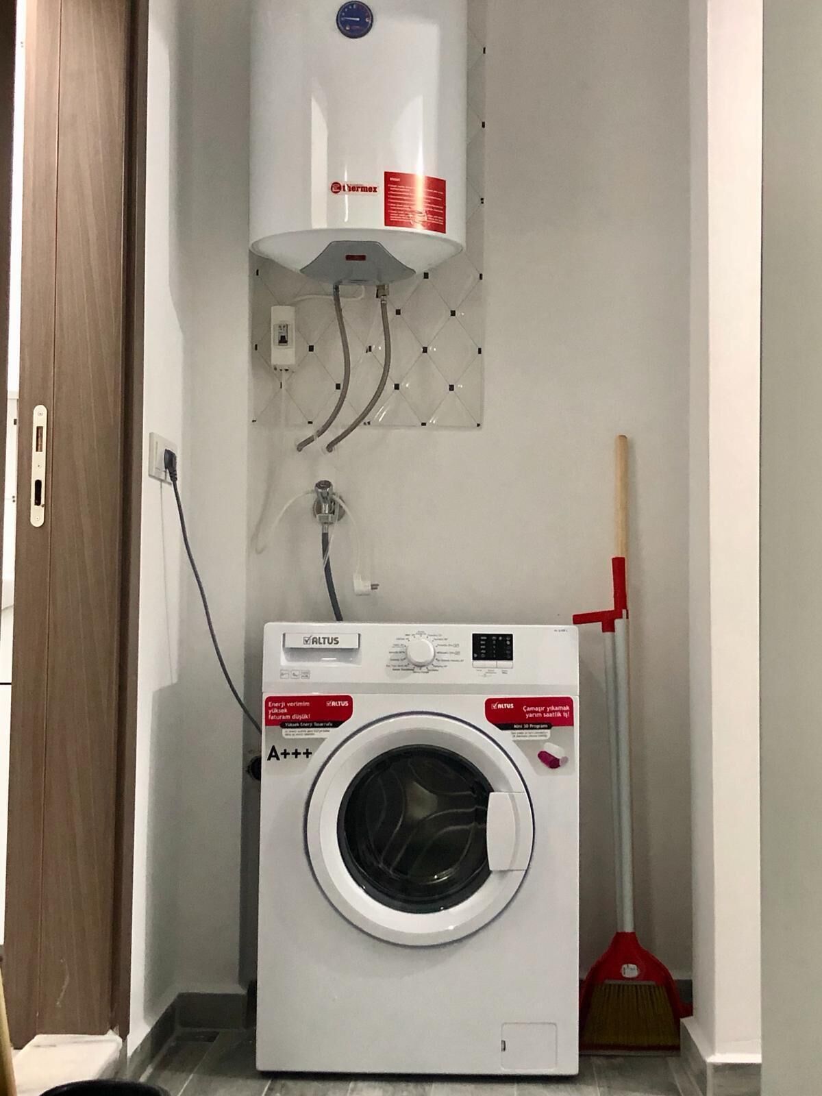 Un espace réduit dédié à la buanderie, comprenant un lave-linge, un chauffe-eau et un balai.