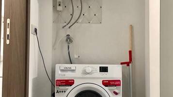 Un espace réduit dédié à la buanderie, comprenant un lave-linge, un chauffe-eau et un balai.