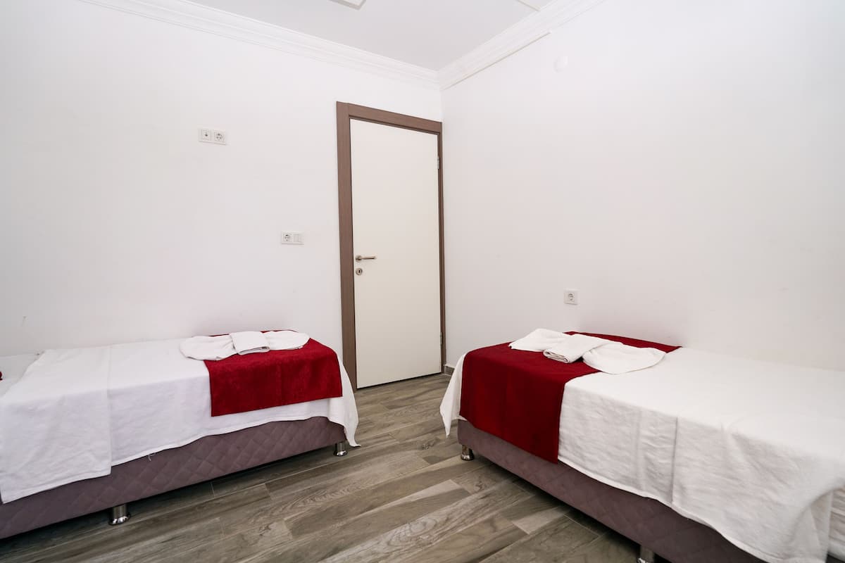 Quarto com duas camas, cada uma com um cobertor vermelho e lençóis brancos, e piso de madeira.