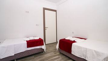 Una habitación con dos camas, cada una con una colcha roja y sábanas blancas, y suelo de madera.