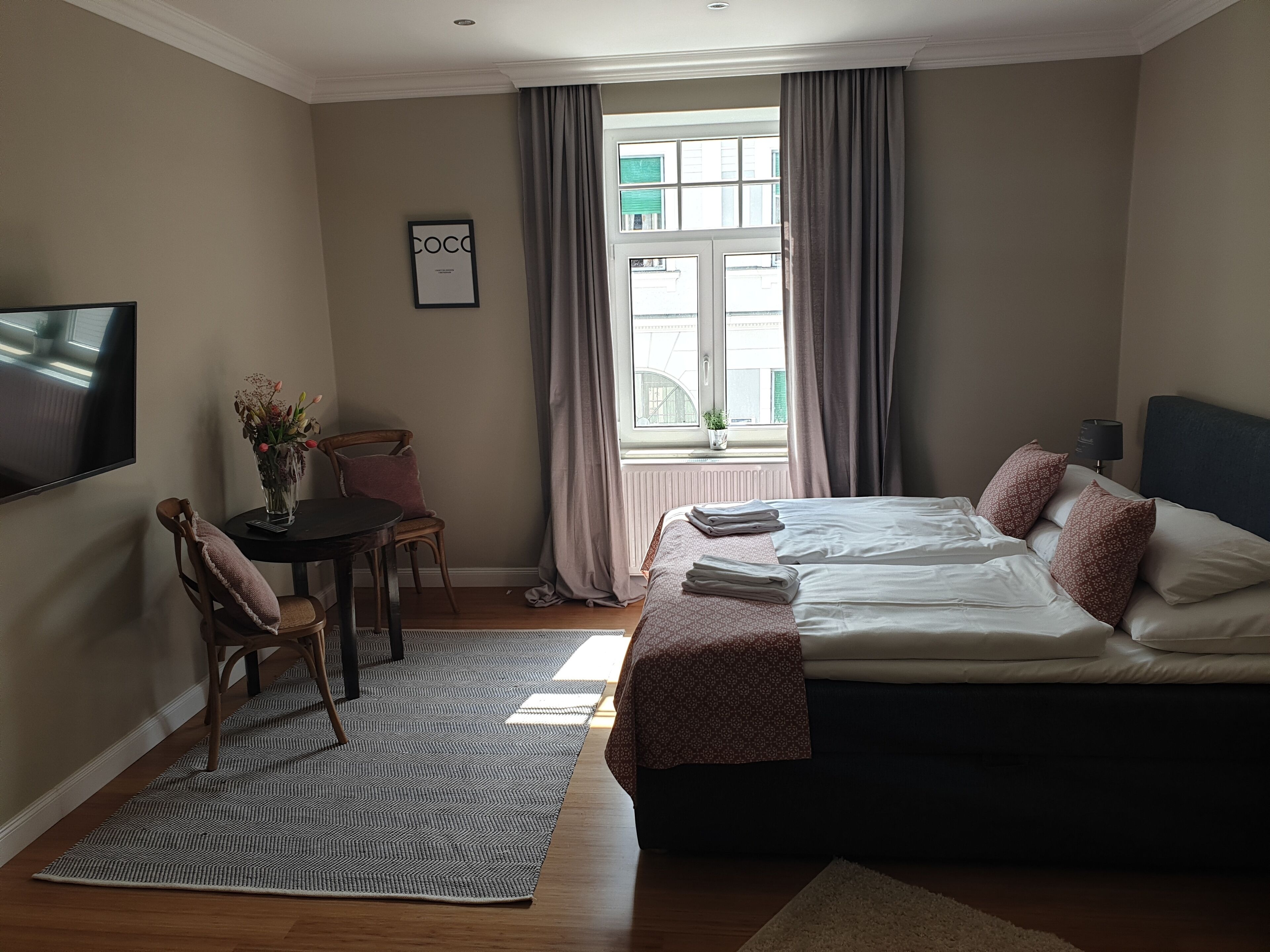 A hotel room with a bed, a desk with a chair, a TV, and a window with curtains.