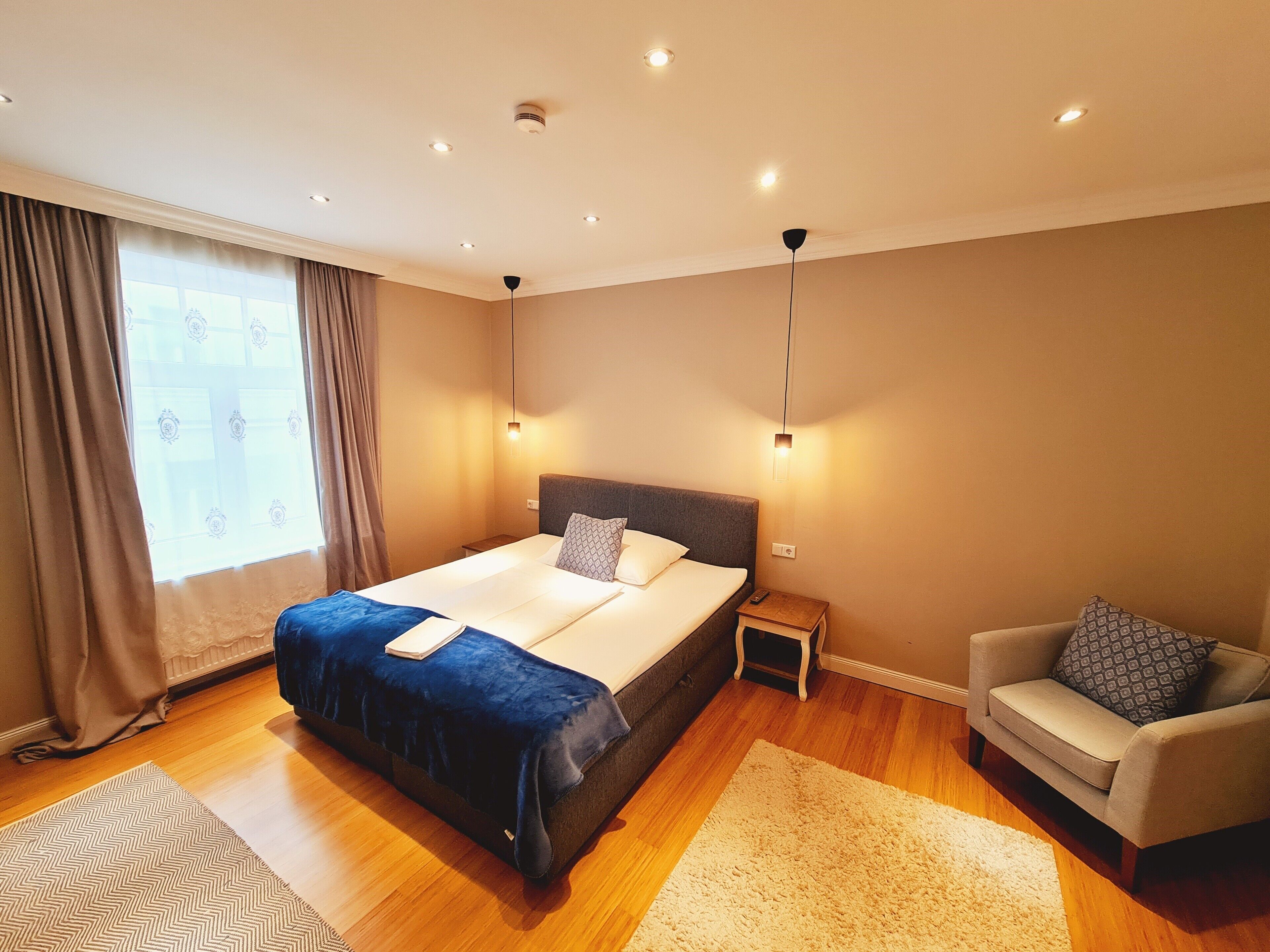 A modern bedroom with a large bed, bedside tables, a chair, and a window with curtains.