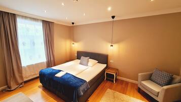 A modern bedroom with a large bed, bedside tables, a chair, and a window with curtains.