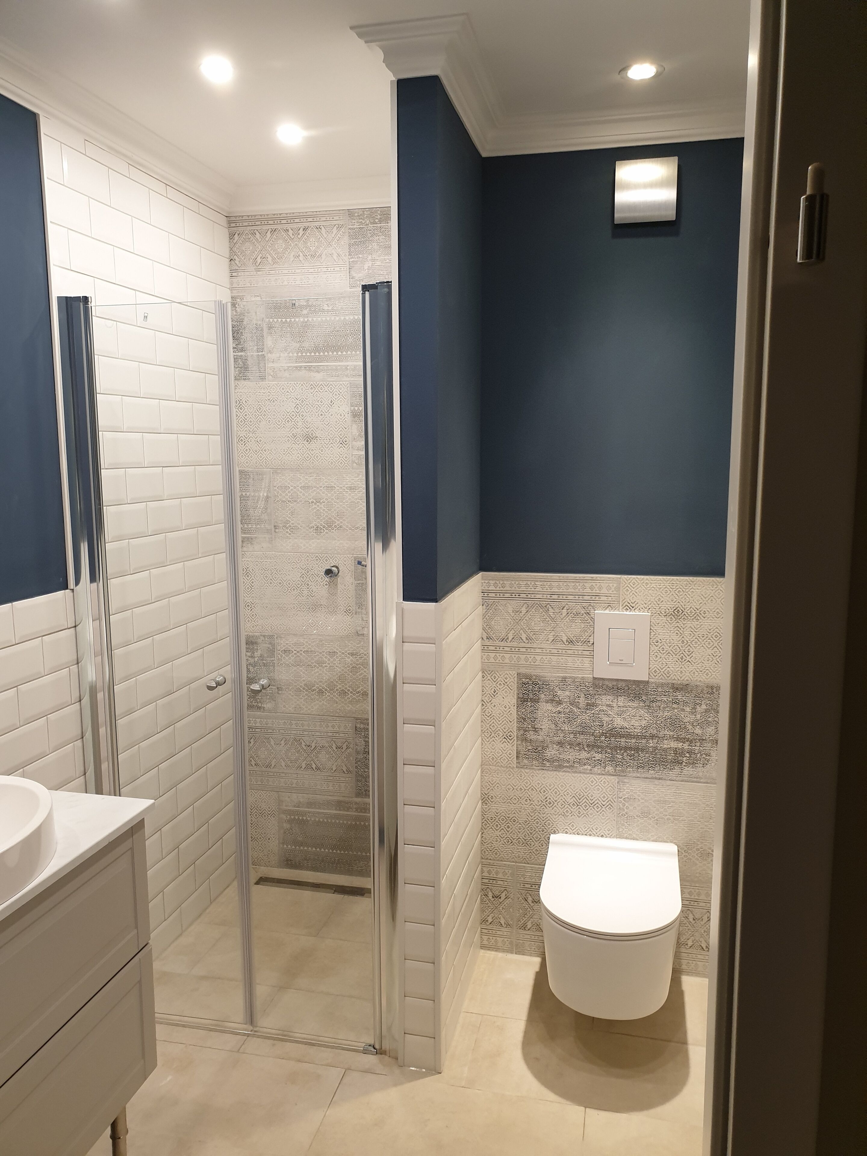A bathroom with a glass-enclosed shower, white tiles, a white sink, and a toilet.