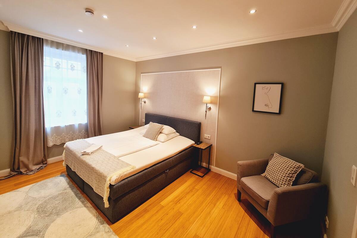 A bedroom with a bed, bedside lamps, a chair, and a window with curtains.