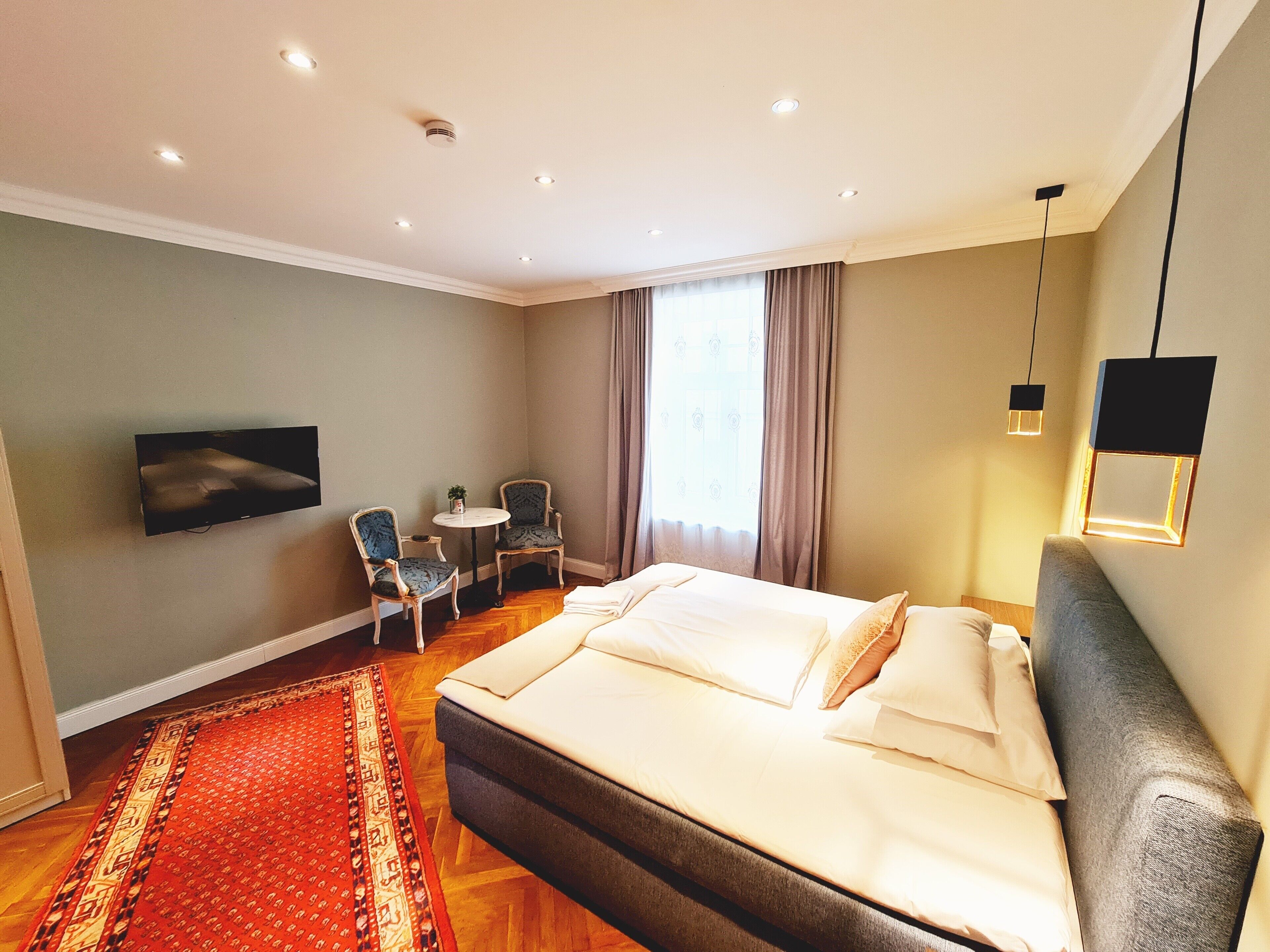 A hotel room with a large bed, a desk with a chair, a television, and a red carpet.