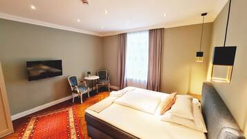 A hotel room with a large bed, a desk with a chair, a television, and a red carpet.