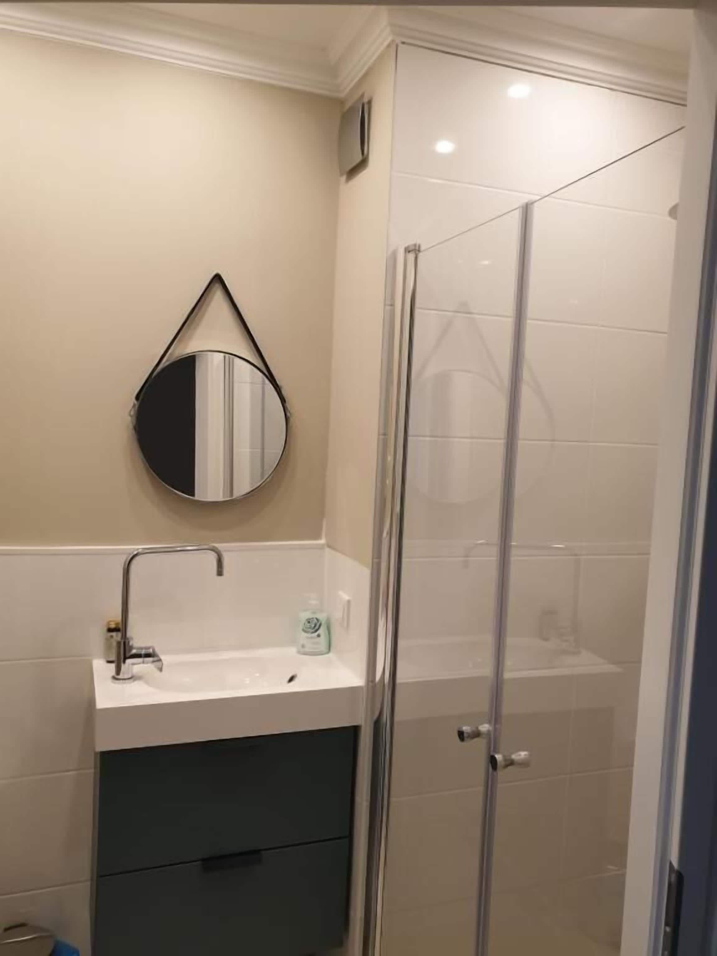 A bathroom with a glass shower enclosure, a sink with a mirror, and a cabinet below.