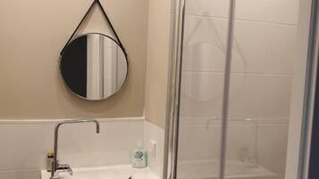 A bathroom with a glass shower enclosure, a sink with a mirror, and a cabinet below.