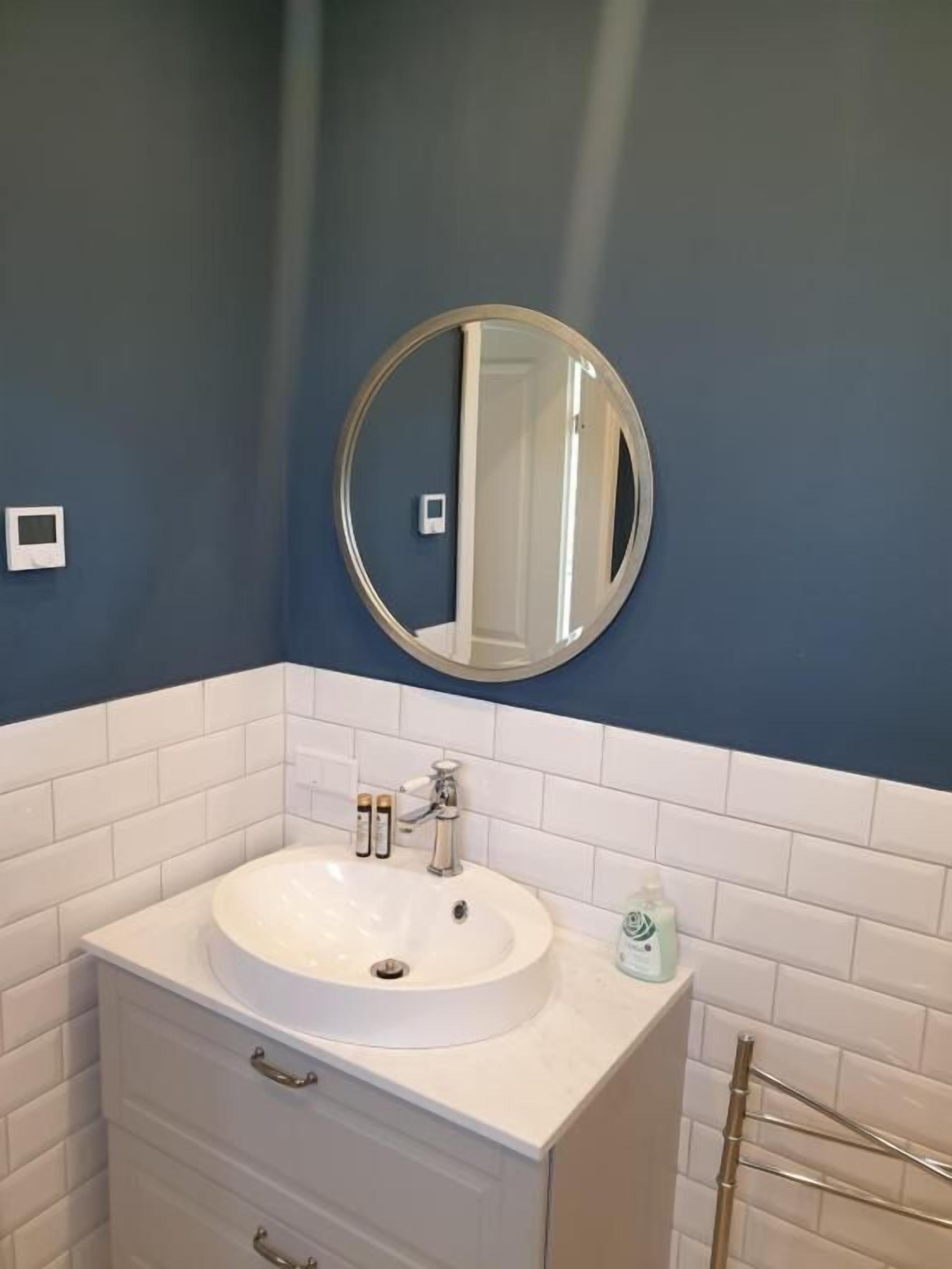 A bathroom with a round mirror, white sink, and a towel rack.
