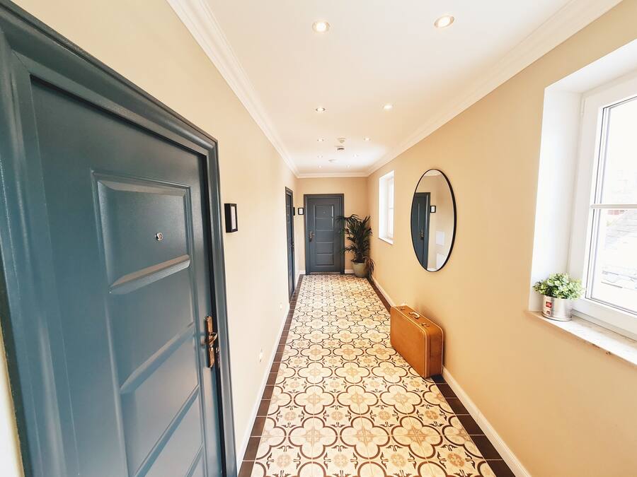 A hallway with patterned flooring, a blue door, a mirror, and a window with a plant.