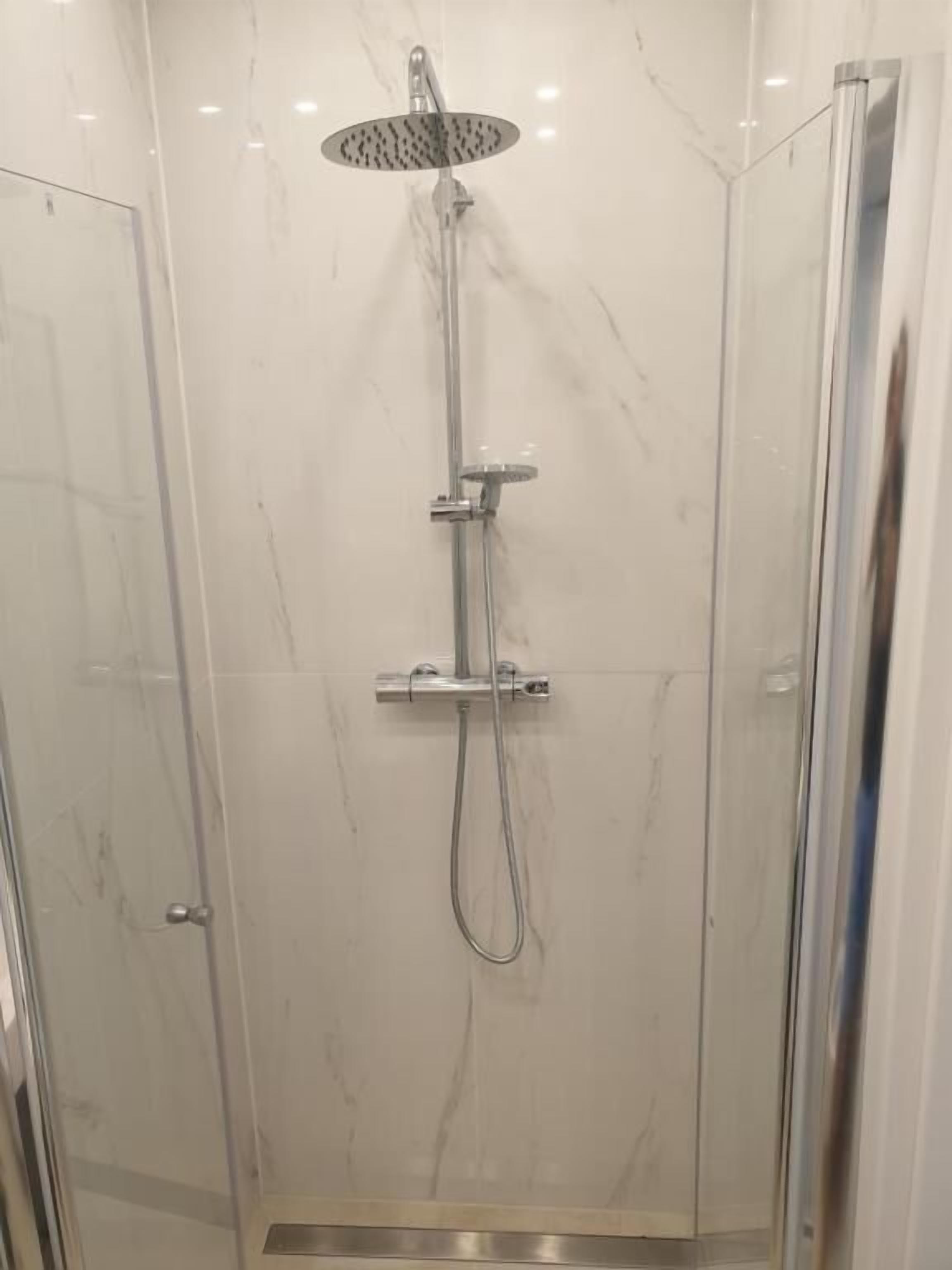 Lasiseinöillä varustettu suihku, jossa on käsisuihku ja seinään asennettu hana.