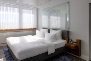 A modern bedroom with a large bed, a bedside table, a wall-mounted mirror, and a window with sheer curtains. - Radisson Blu Erfurt (Erfurt)