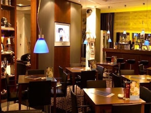 Eine Hotelhalle mit mehreren Tischen und Stühlen, einem Barbereich und einem großen Bild in einem Rahmen an der Wand.