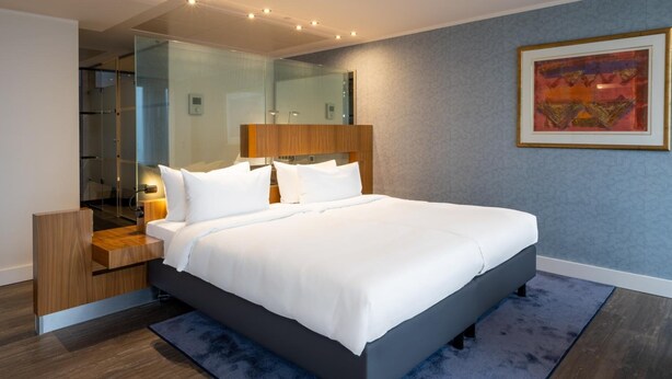 A modern hotel room with a large bed, a bedside table, a mirror, and a framed artwork on the wall. - Radisson Blu Erfurt (Erfurt)