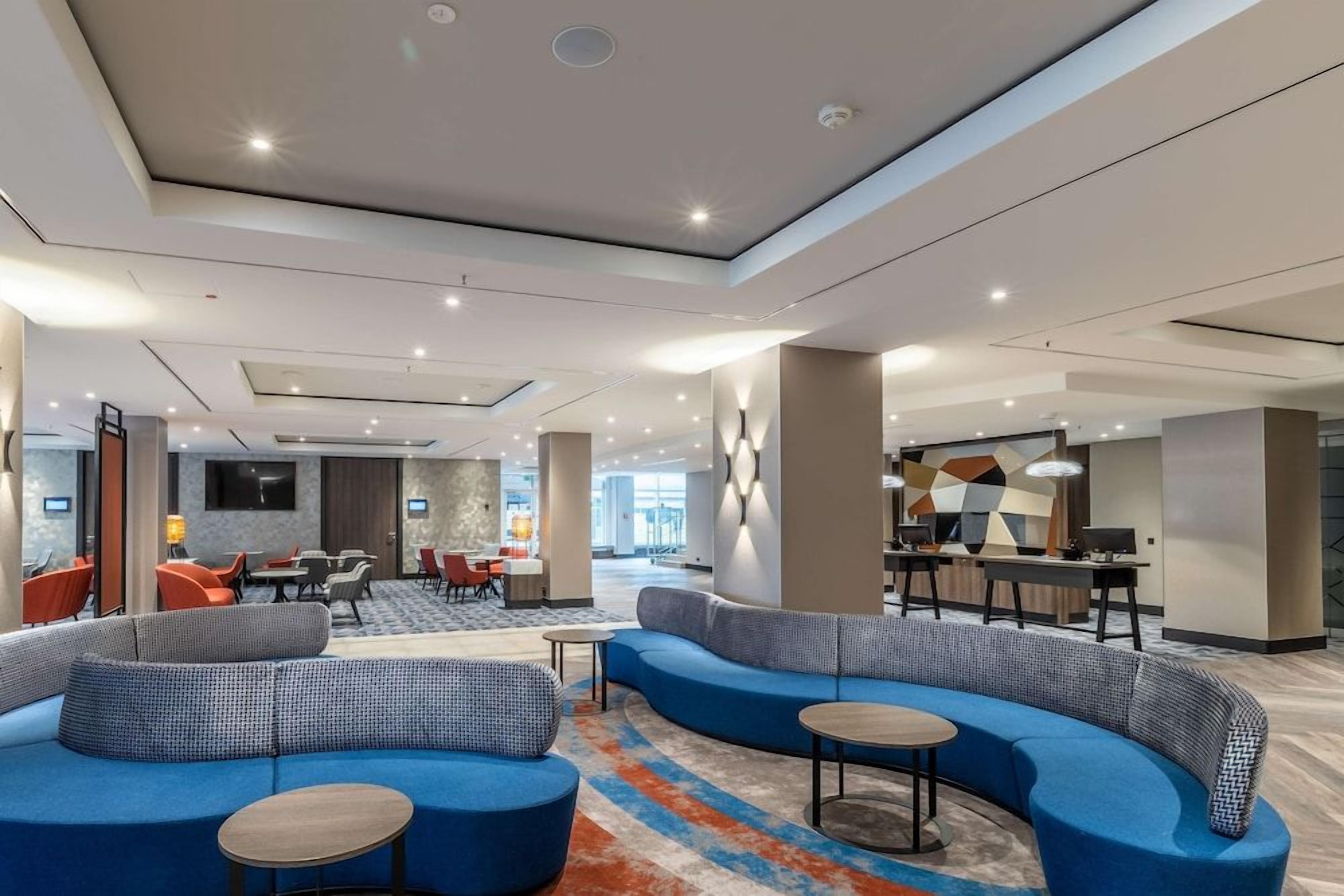 Eine moderne Hotellobby mit einer gebogenen blauen Sofaecke, einer Bar und einem Essbereich.