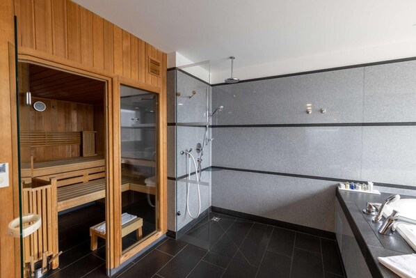 Ein modernes Badezimmer mit Sauna, einer Glaskabinentrennung zur Dusche und einem Waschbecken-Möbel.