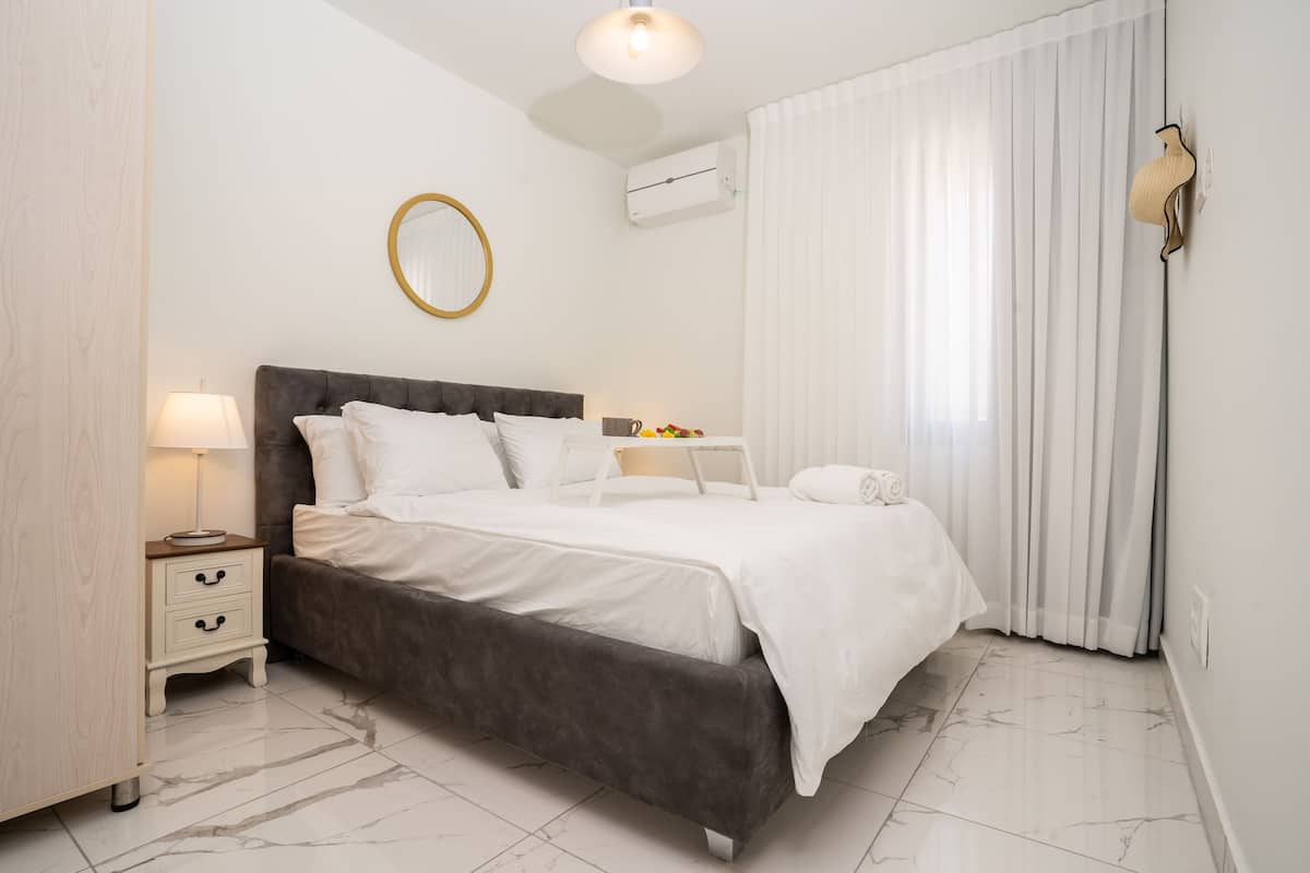 Une chambre moderne avec un grand lit, des tables de chevet, un miroir et une fenêtre avec des rideaux.
