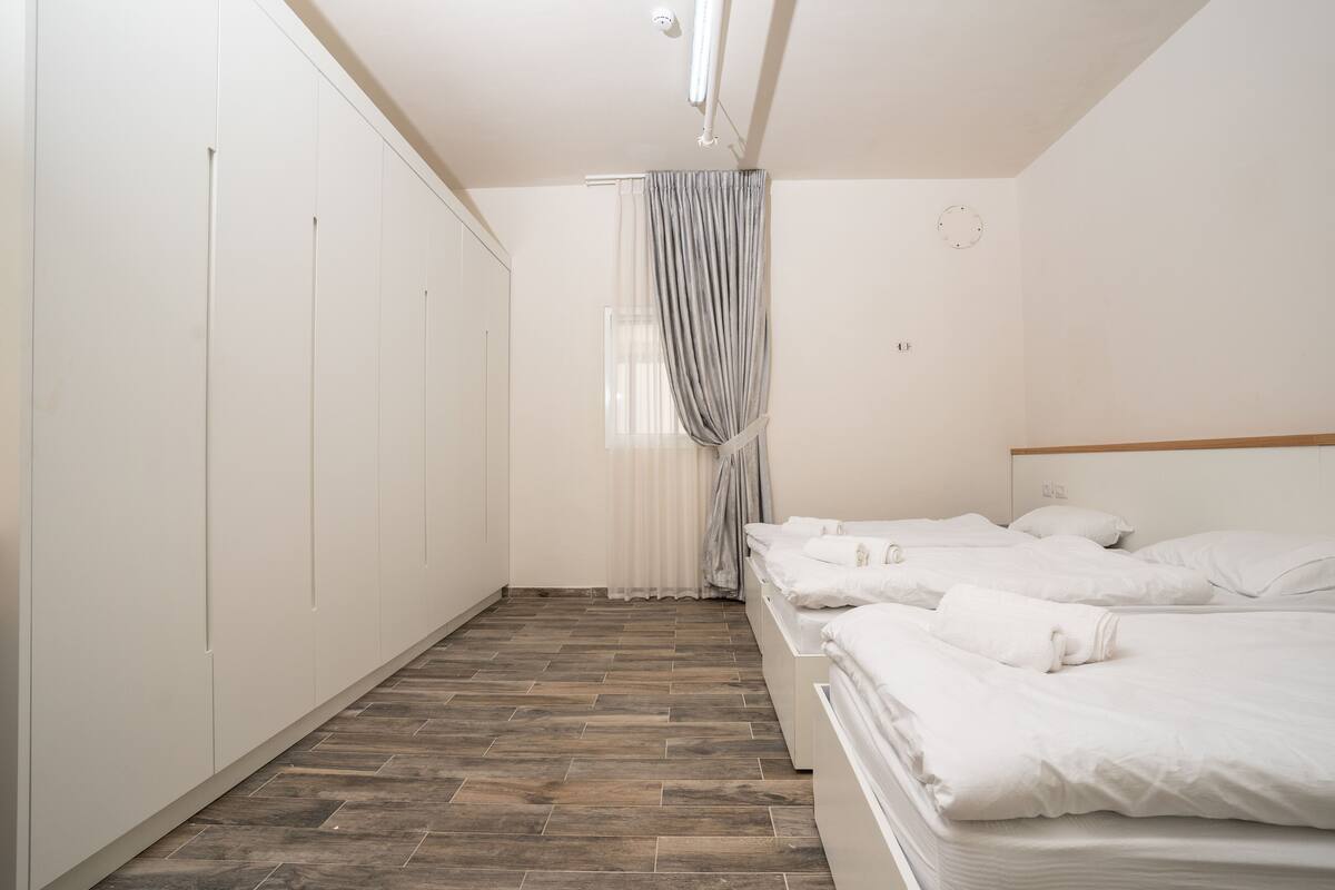 Une chambre avec deux lits, une armoire, une fenêtre avec des rideaux et une horloge au mur.