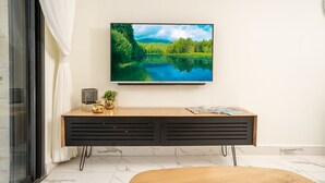 Uma sala de estar moderna com uma televisão de tela plana fixada na parede, uma mesa de console de madeira com objetos decorativos e um chão de mármore.