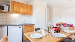 Una cocina compacta con armarios de madera, microondas y lavavajillas. Una mesa de comedor está dispuesta con platos, vasos y cubiertos.