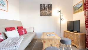Una habitación acogedora con sofá, televisión, mesa de madera y una silla.