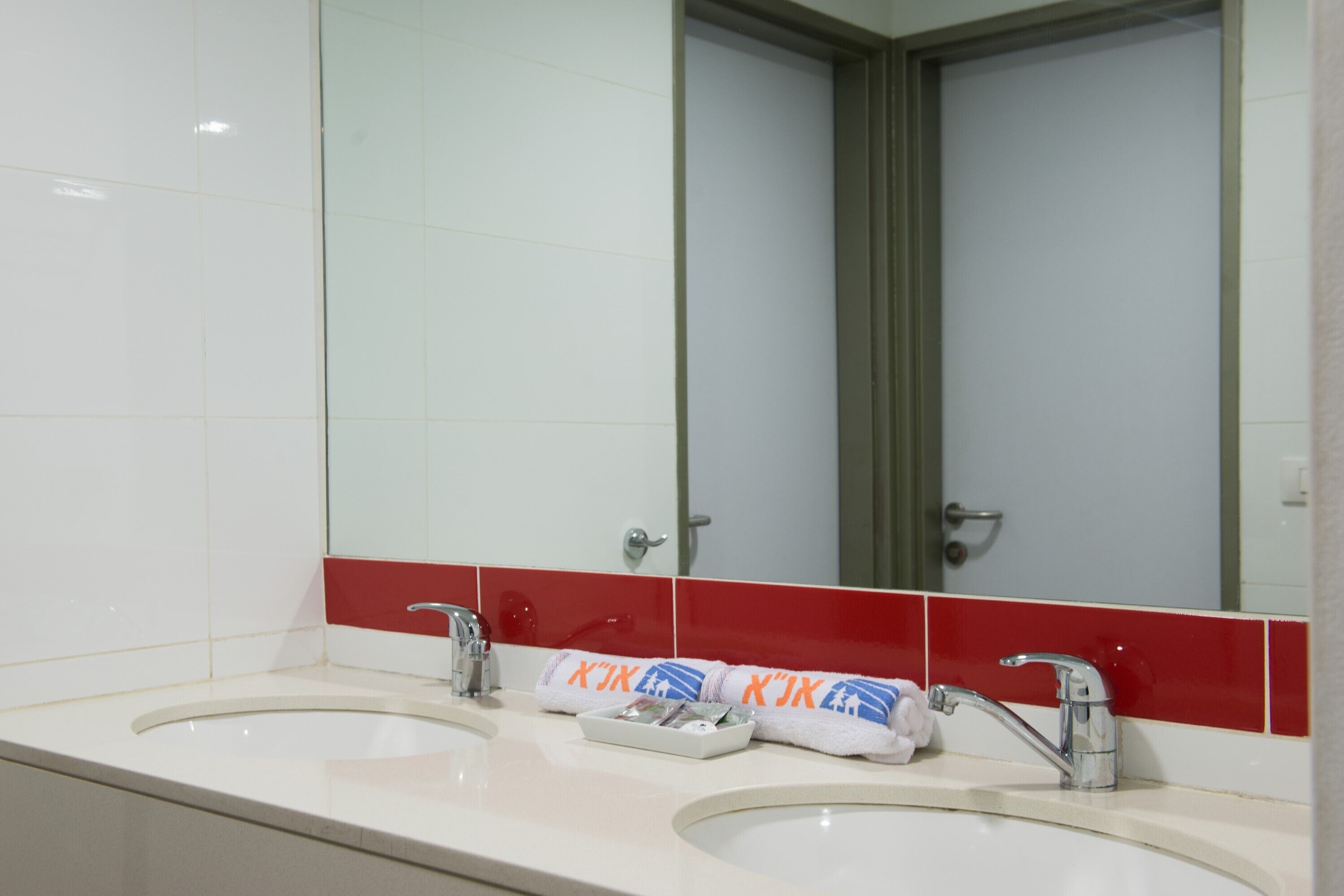 Un baño con dos lavamanos, un espejo y un toallero con toallas.