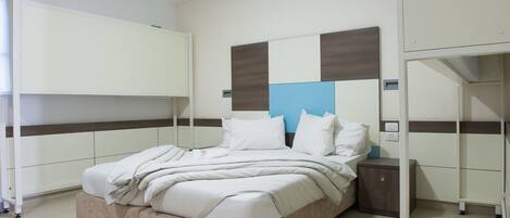 Una cama bien hecha con ropa blanca, una mesita de noche con lámpara y un armario empotrado en la pared.