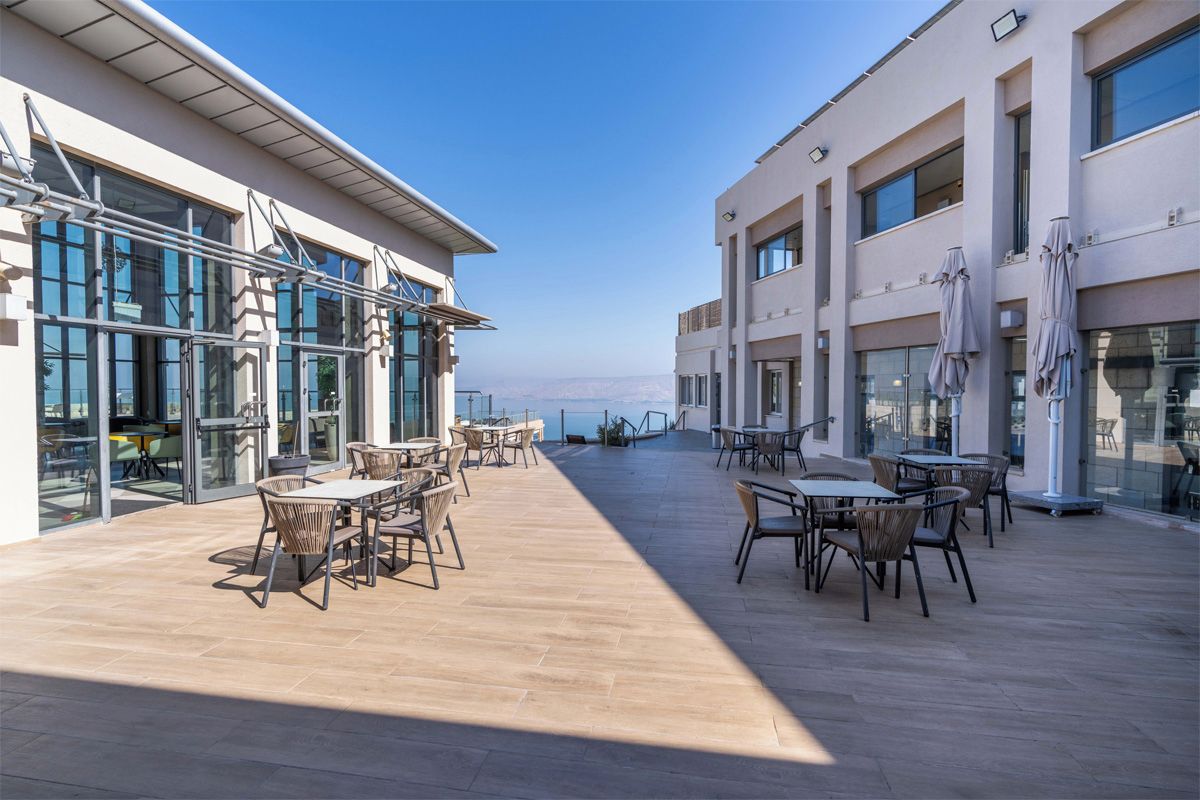 An outdoor patio area with tables and chairs, large windows, and a view of the sea.