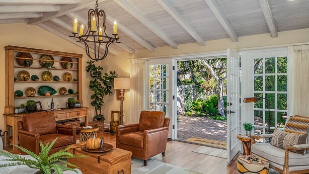 A spacious living room with a chandelier, leather armchairs, a wooden coffee table, and a large window offering a view of the garden.